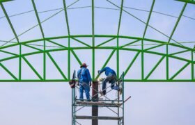 Two construction workers on scaffolding working to build metal roof structure of industrial building